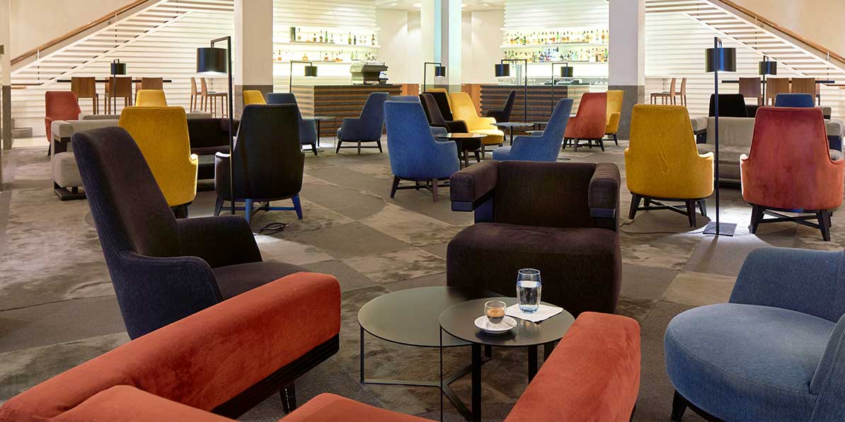 Das Bild zeigt eine moderne und stilvolle Loungebar mit vielen farbenfrohen Sesseln und Sofas, die in Gruppen angeordnet sind.